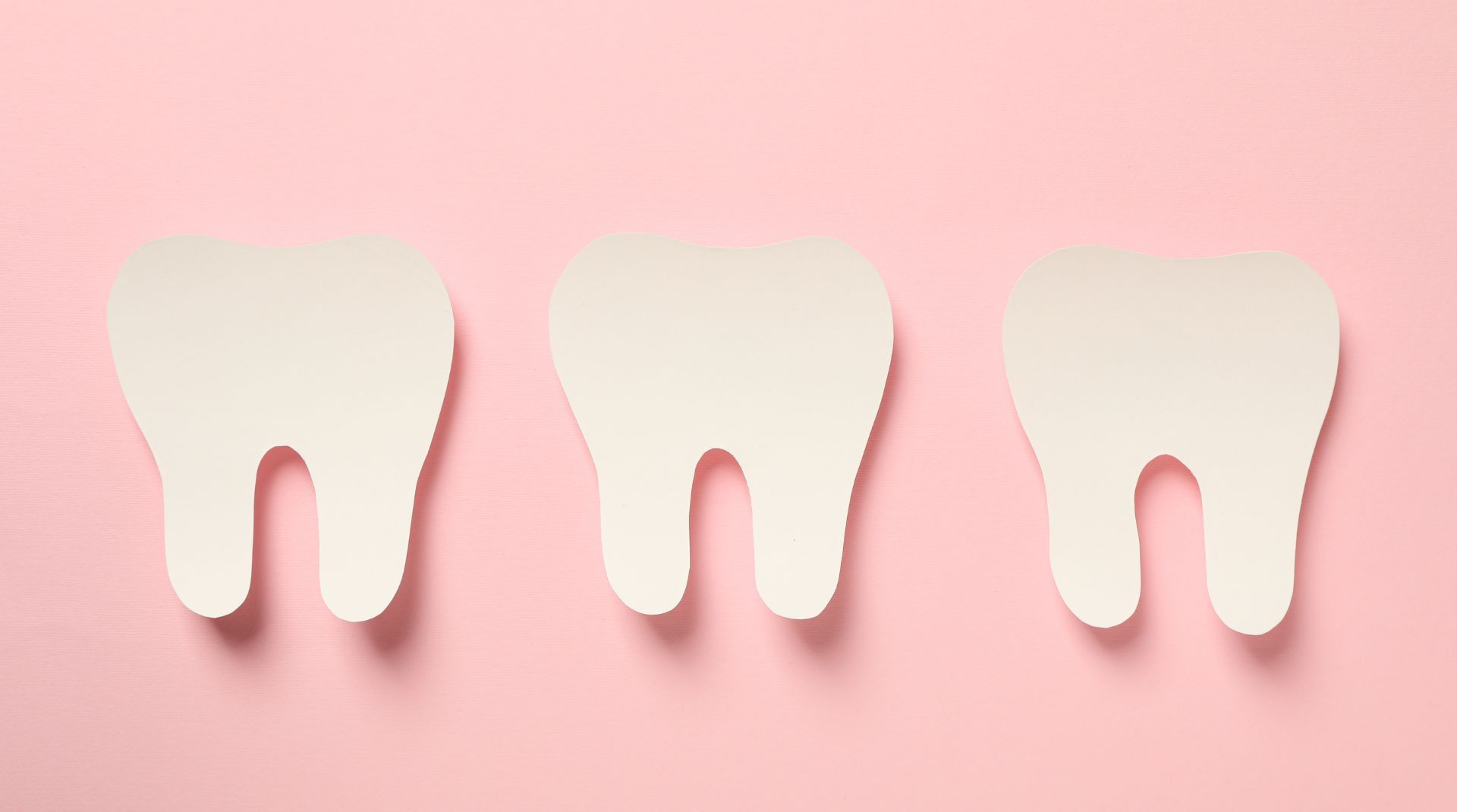 Three white paper tooth cutouts on a pink background.