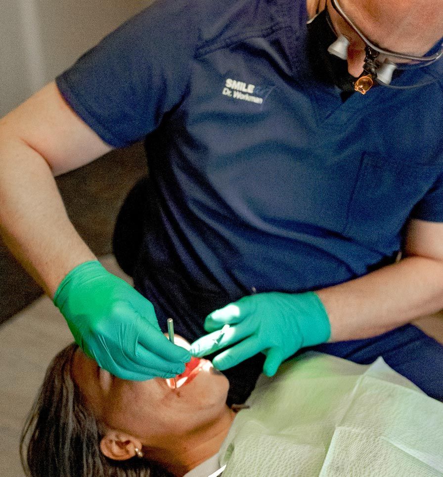 SmileArt Utah examining patient's teeth. Dentist wears green gloves, scrubs, and magnification glasses.