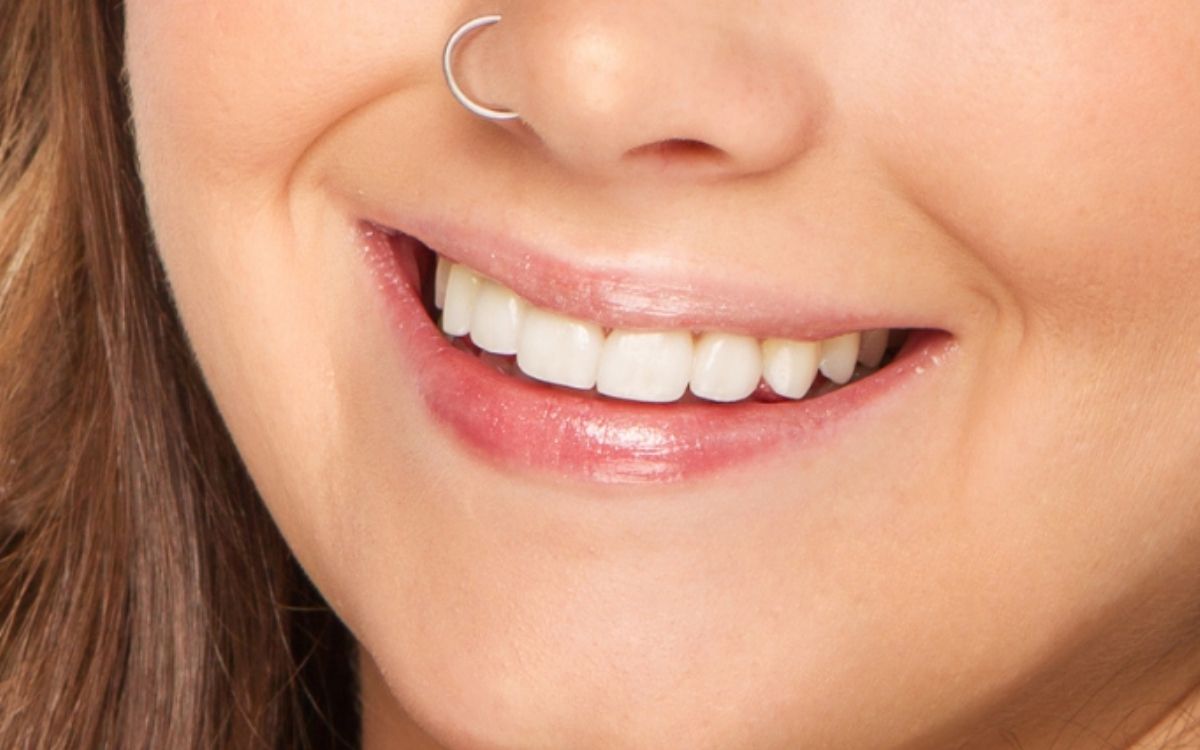 Close-up of a smiling person with a nose ring and pearly white teeth.