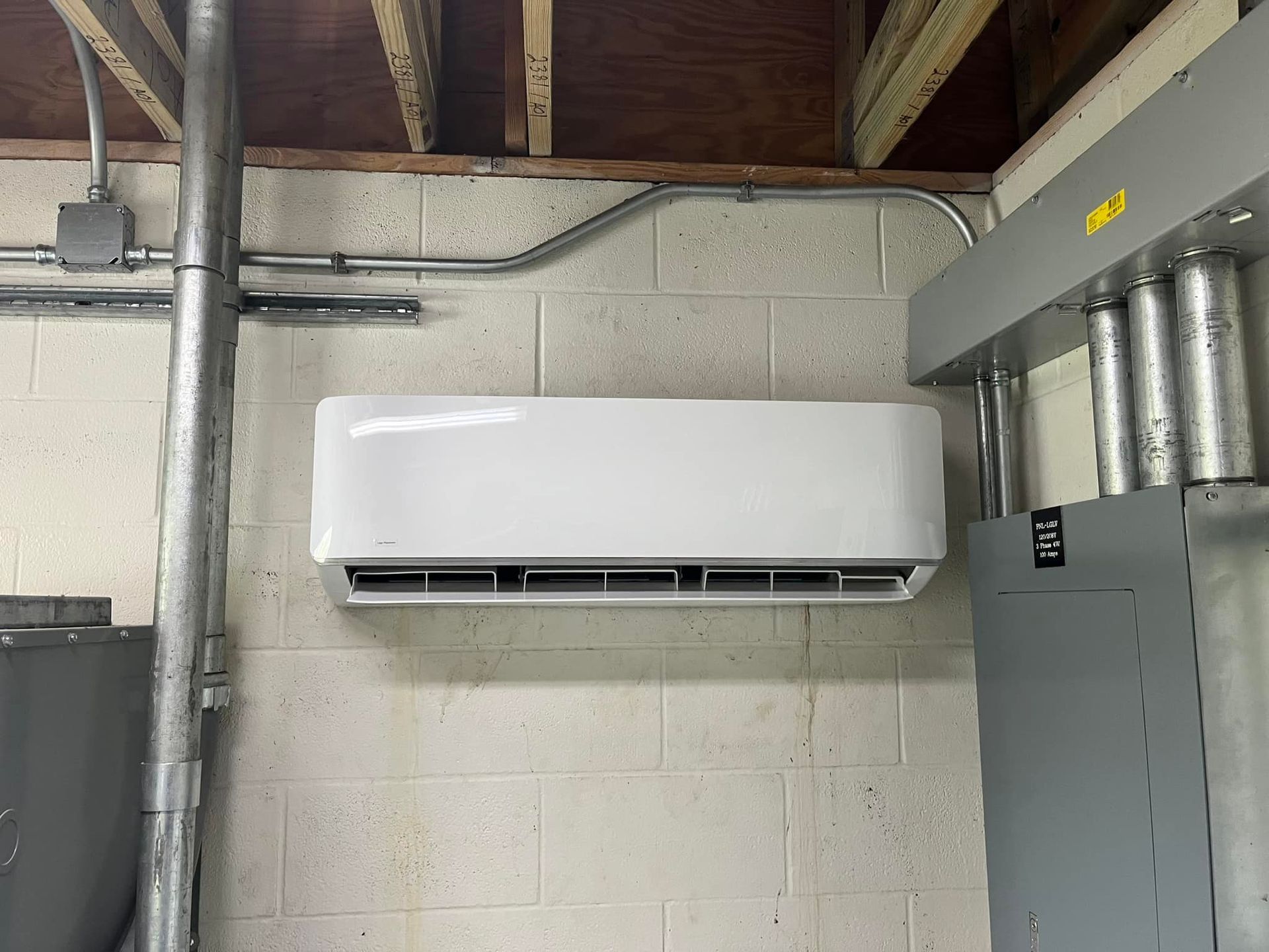 A white air conditioner is hanging on a brick wall in a room.