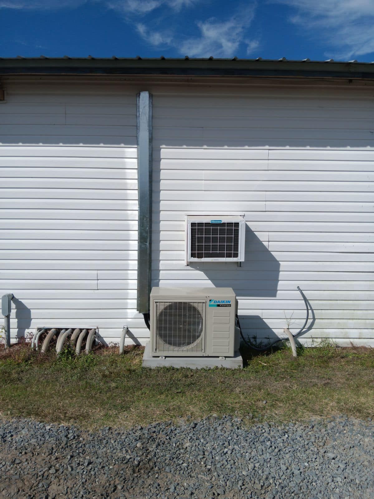 A small air conditioner is sitting on the side of a white building.