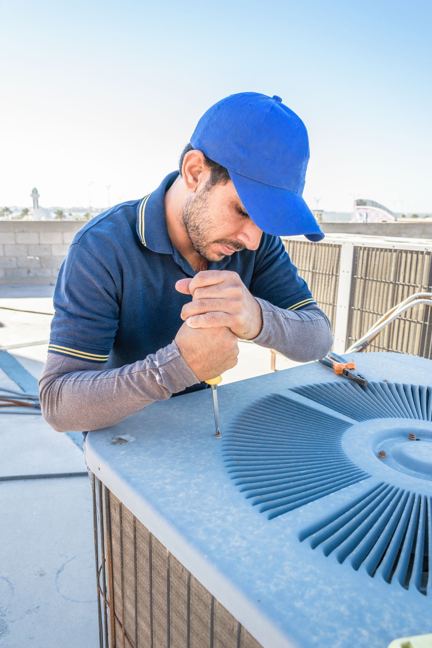A man in a blue hat is working on an air conditioner.