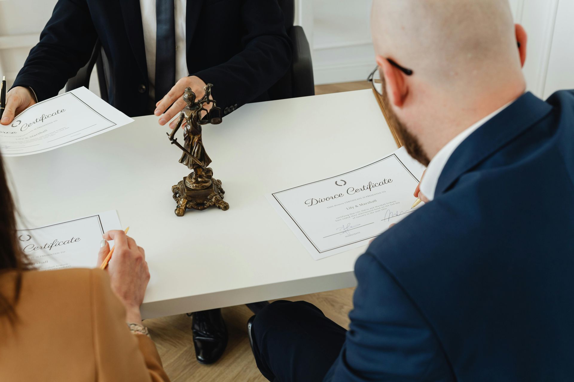 Three people in a meeting around a table with papers and a small statue centerpiece
