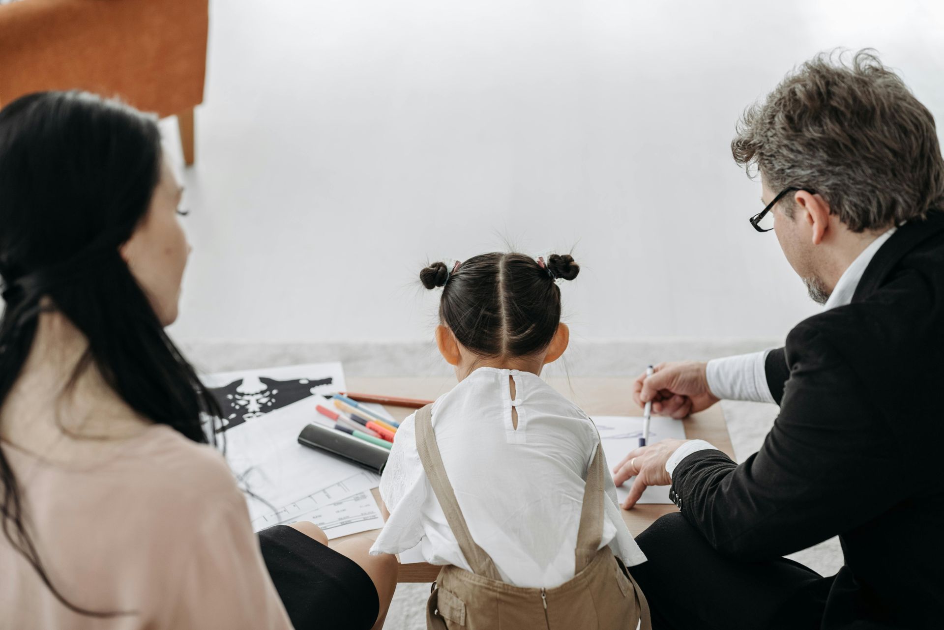 Three people sit at a table, reviewing papers during a meeting in a bright room.