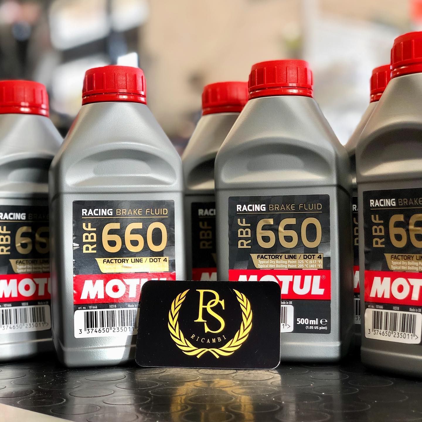Diverse bottiglie di liquido freni da competizione Motul RBF 660, disposte insieme a un piccolo cartoncino nero con un logo dorato al centro.