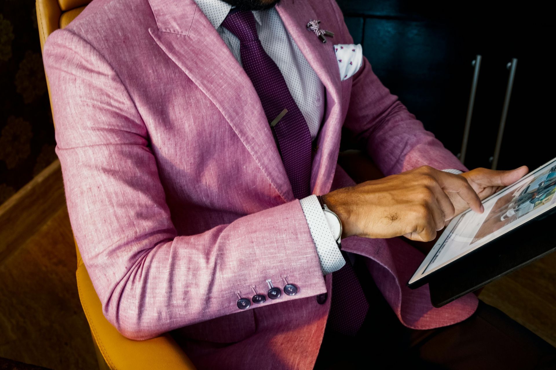 A man in a pink suit and tie is sitting in a chair reading a book.