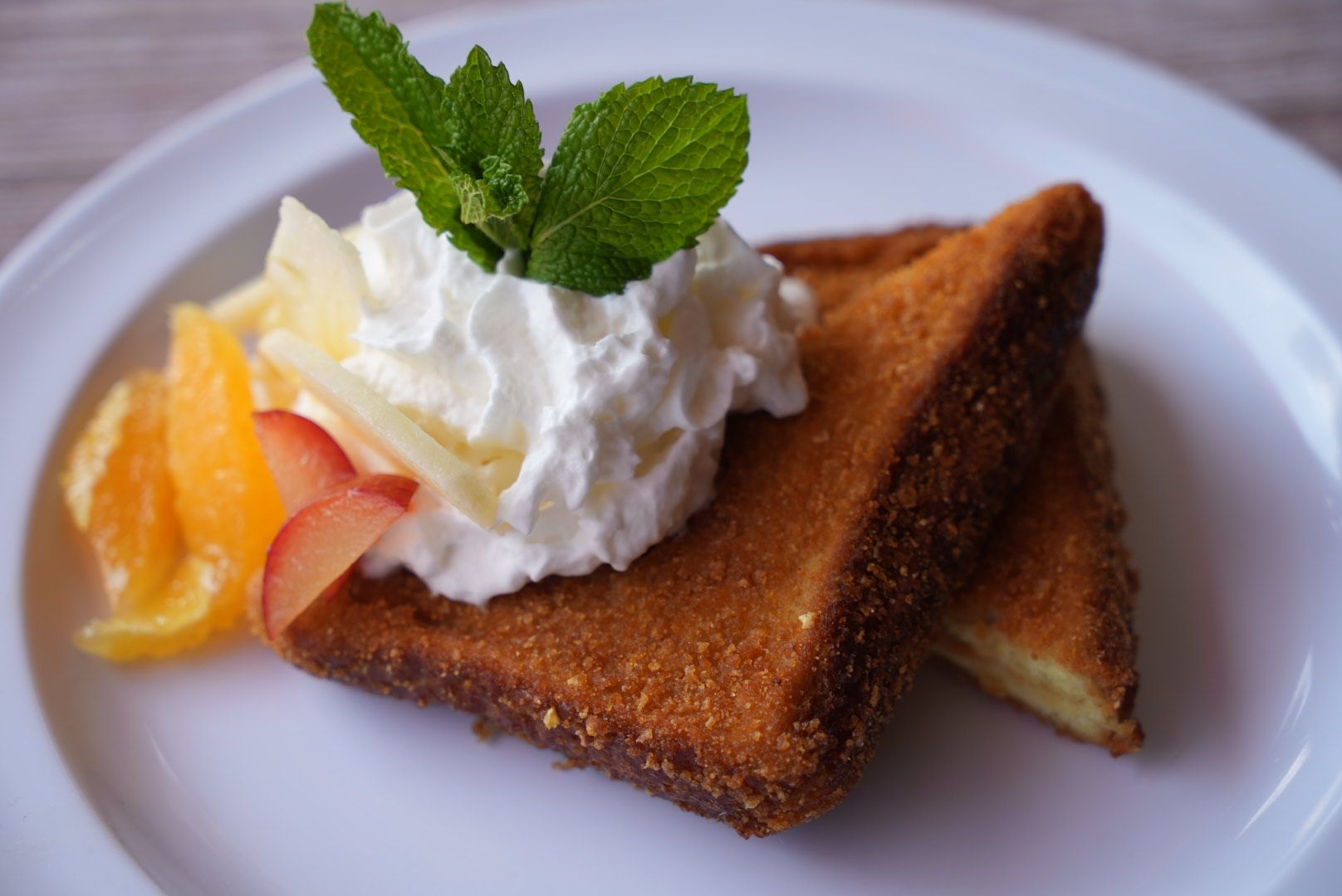 Golden fried bread with whipped cream, mint, and fruit on a white plate.