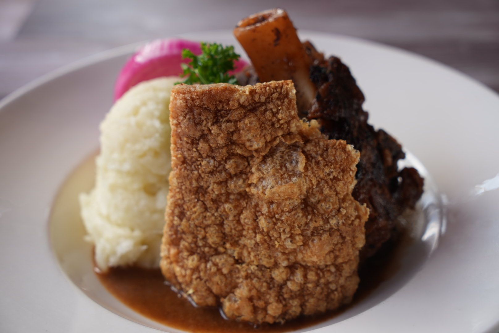 Plate with pork belly, mashed potatoes, meat, pickled onion, and gravy.