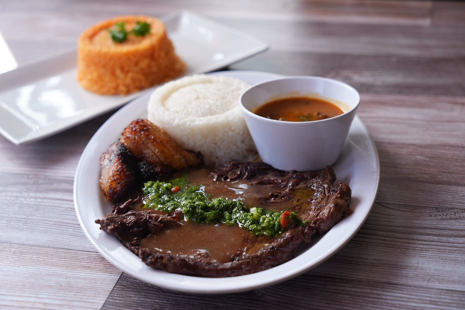 Plate of food with steak, rice, sauce, and a side dish.