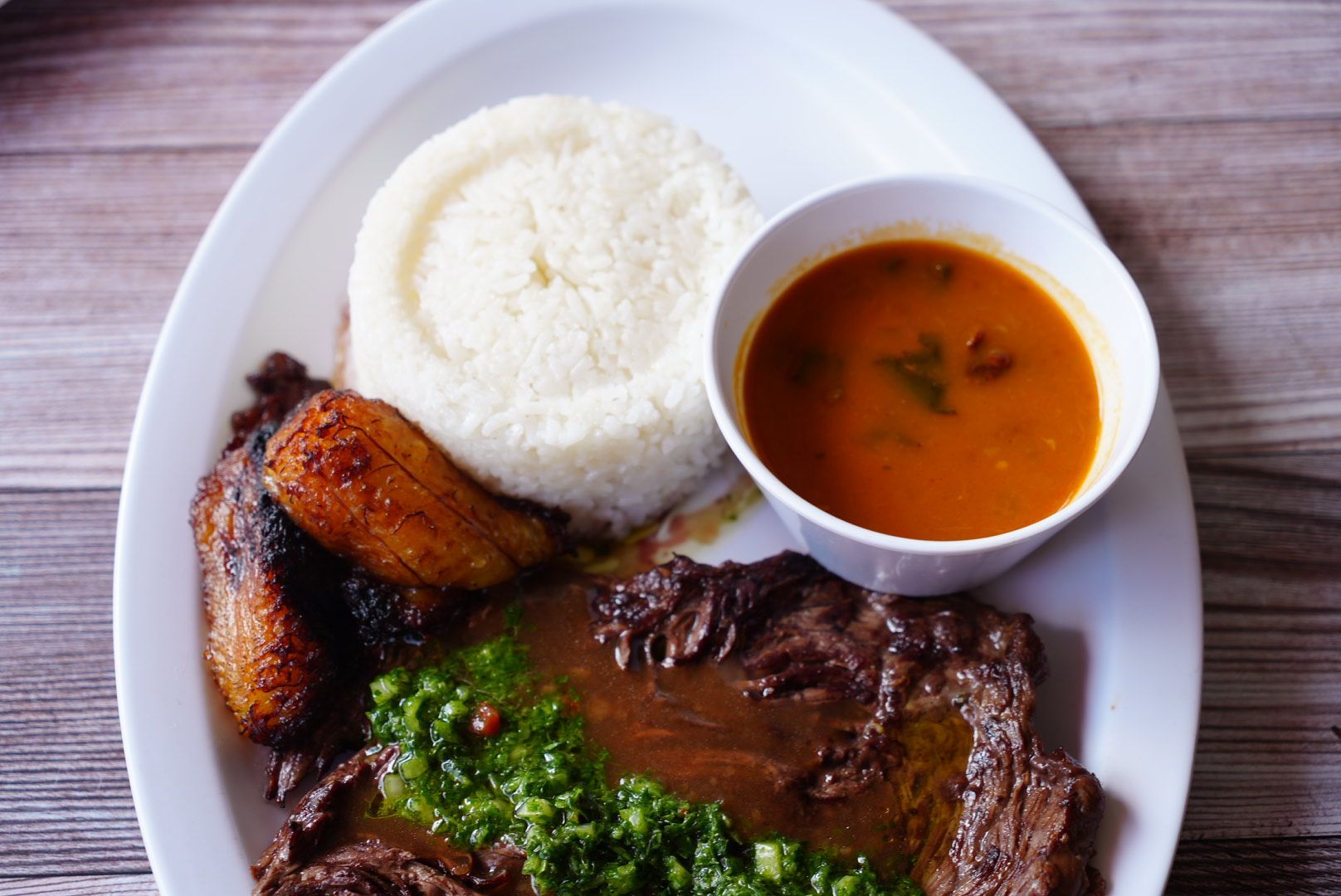 Plate with rice, plantains, steak with green sauce, and a bowl of soup.