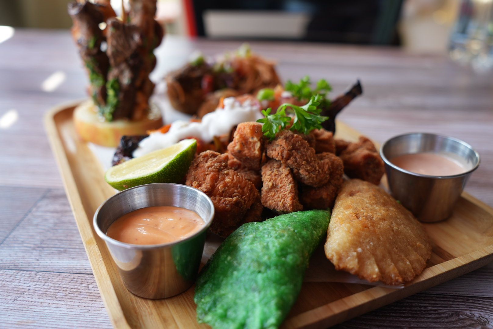 Wooden tray of diverse fried appetizers with dipping sauces.