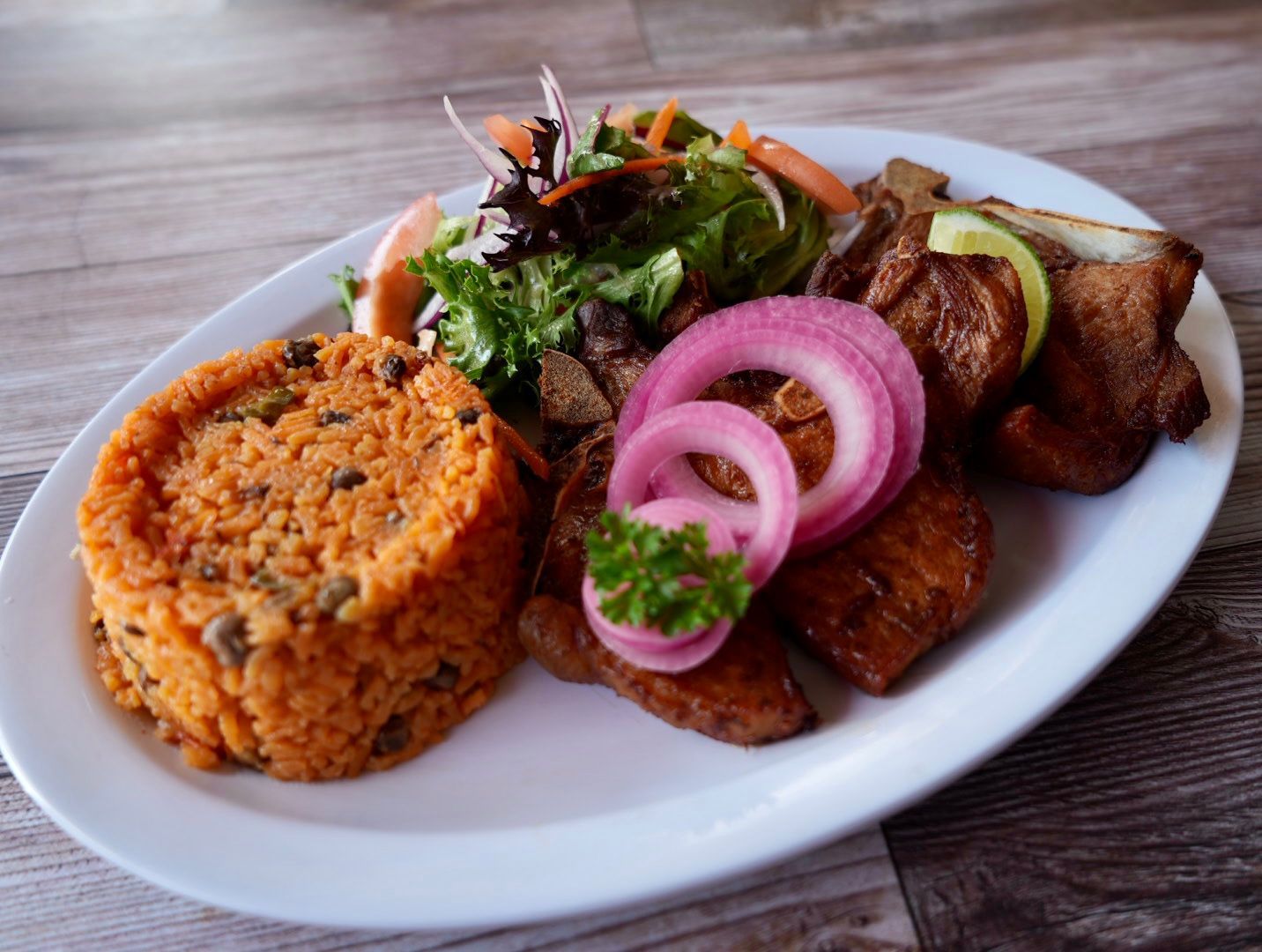 Plate of food: rice, salad, meat, onion rings, and fried plantains.