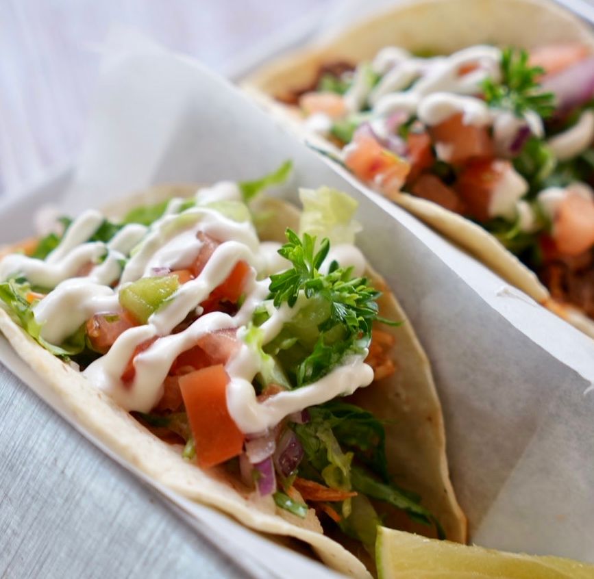 Tacos with toppings, including sauce, lettuce, and tomatoes. Presented on paper.