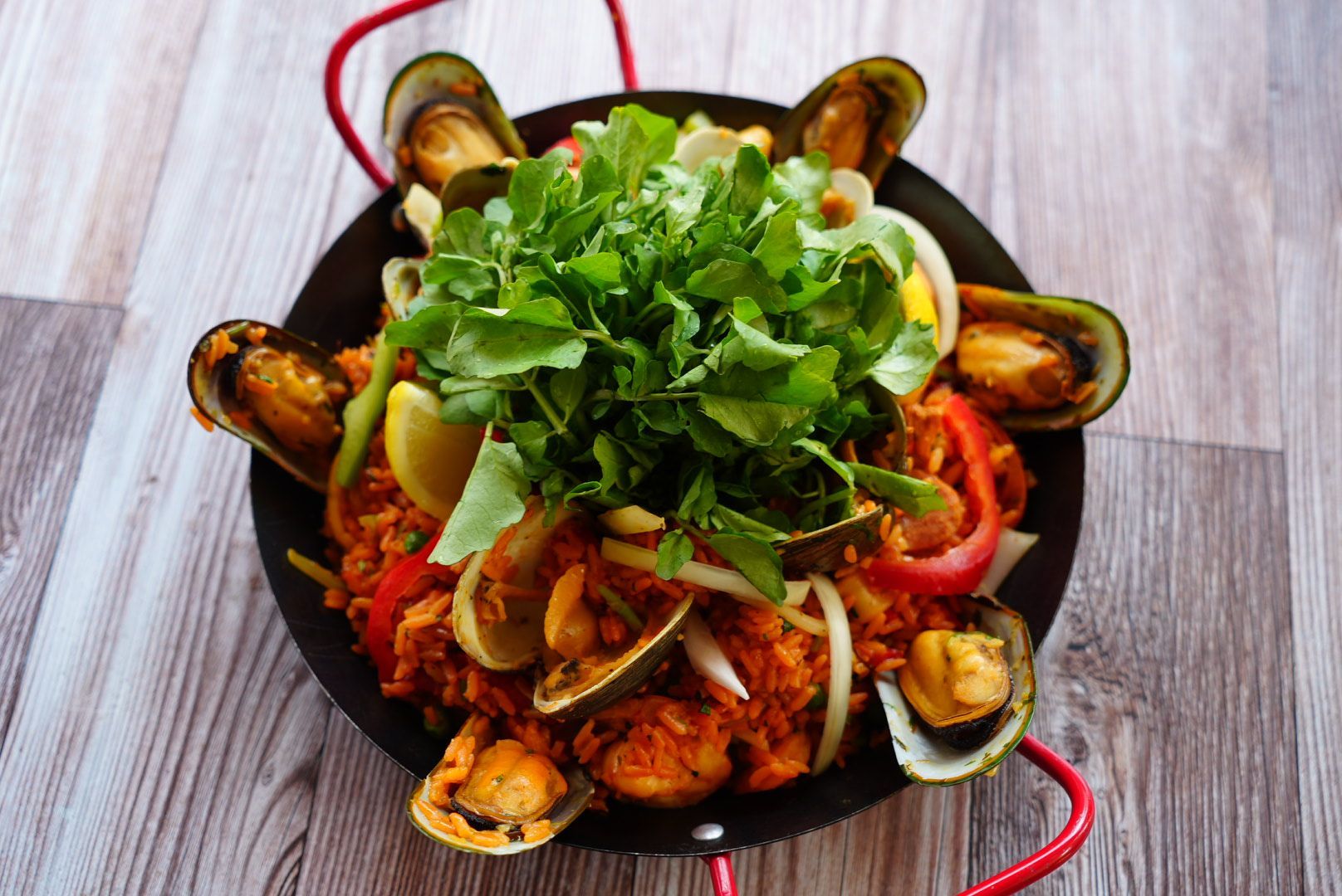 Paella with mussels, clams, and arugula on a wooden table.