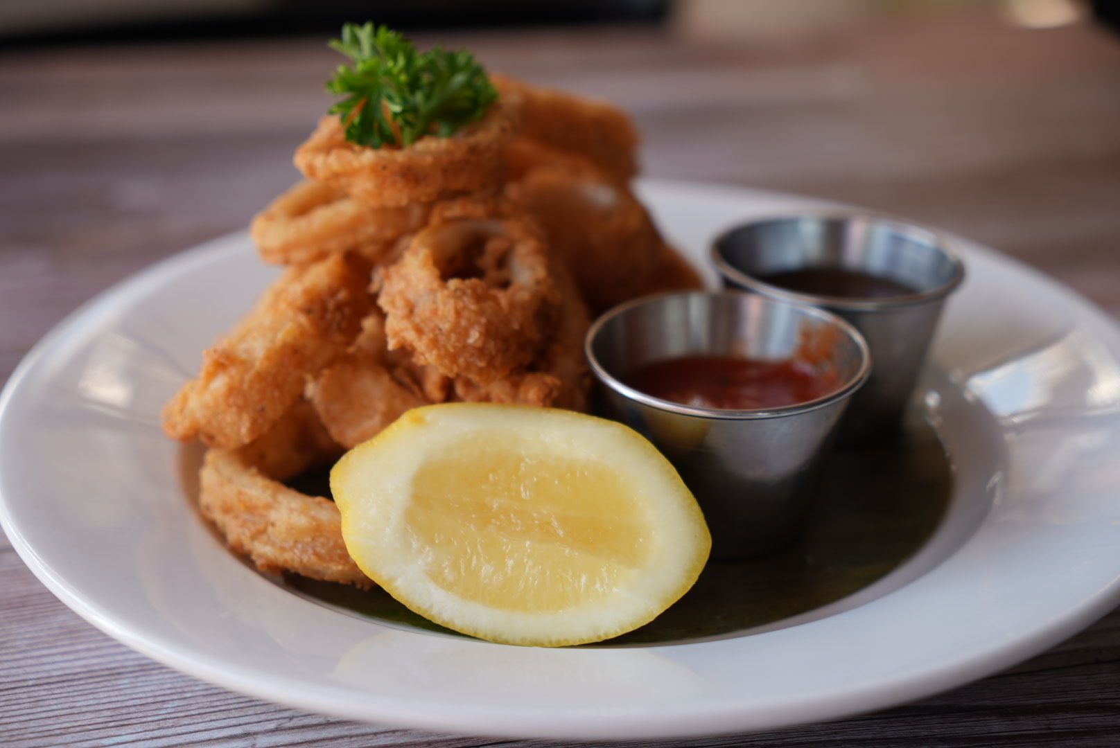 Fried calamari rings on a white plate with lemon, parsley, and dipping sauces.