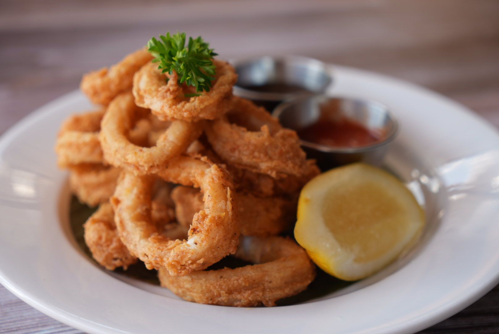 Plate of fried calamari rings with dipping sauces and lemon wedge.