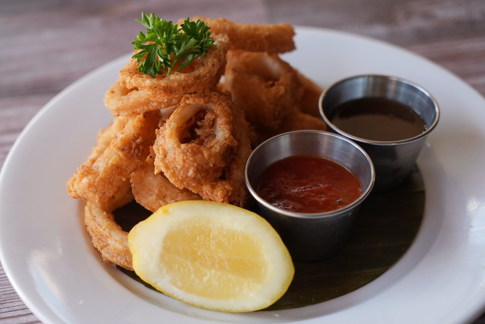 Fried calamari with dipping sauces and a lemon wedge on a white plate.