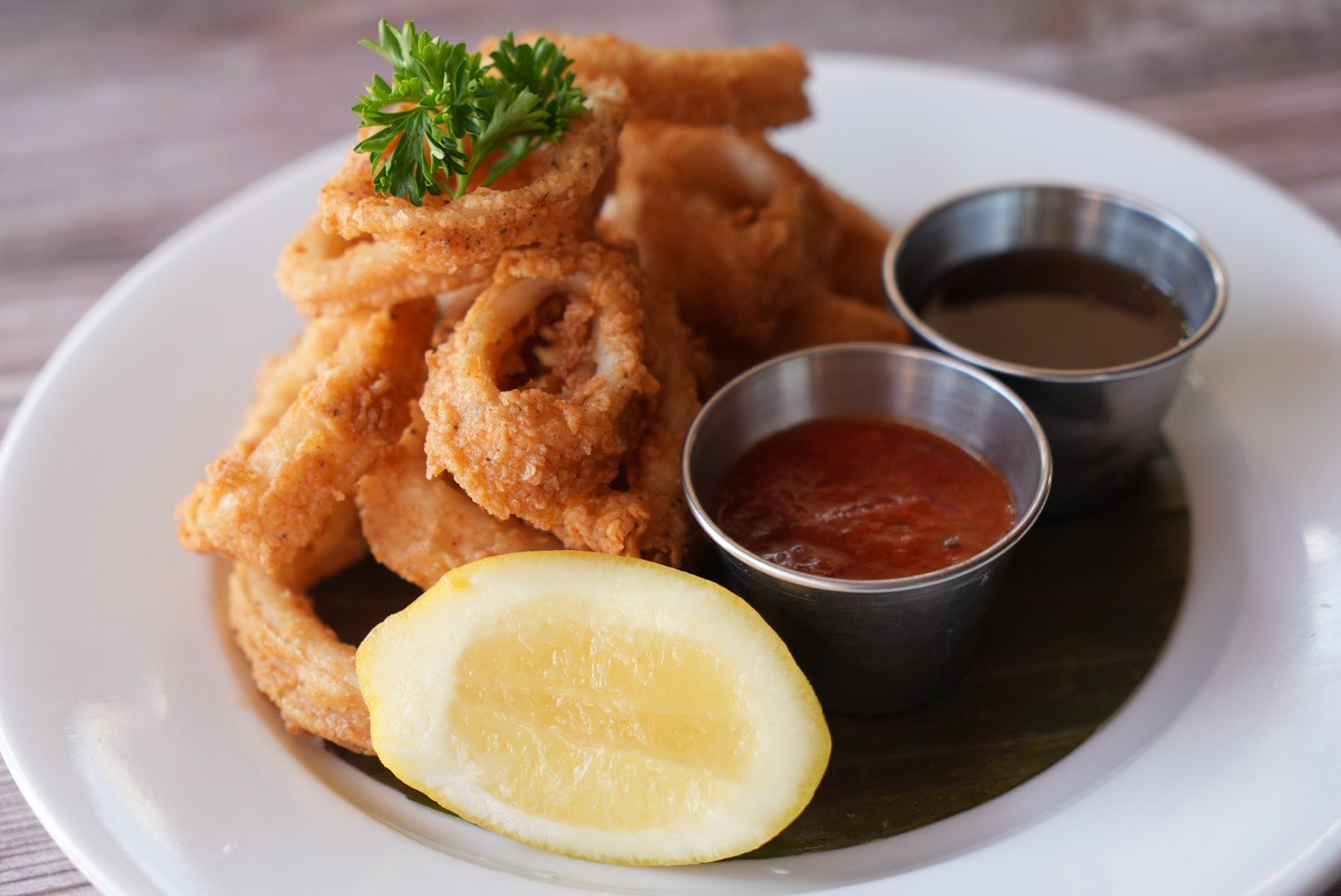 Plate of fried calamari rings with dipping sauces and lemon.