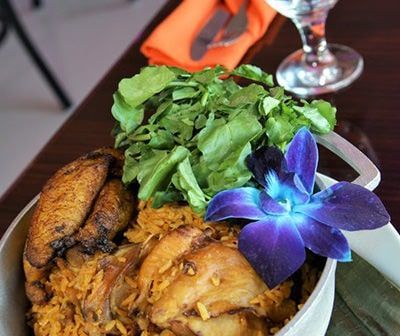 Plate of food with fried plantains, yellow rice, green leafy greens, and a blue flower.