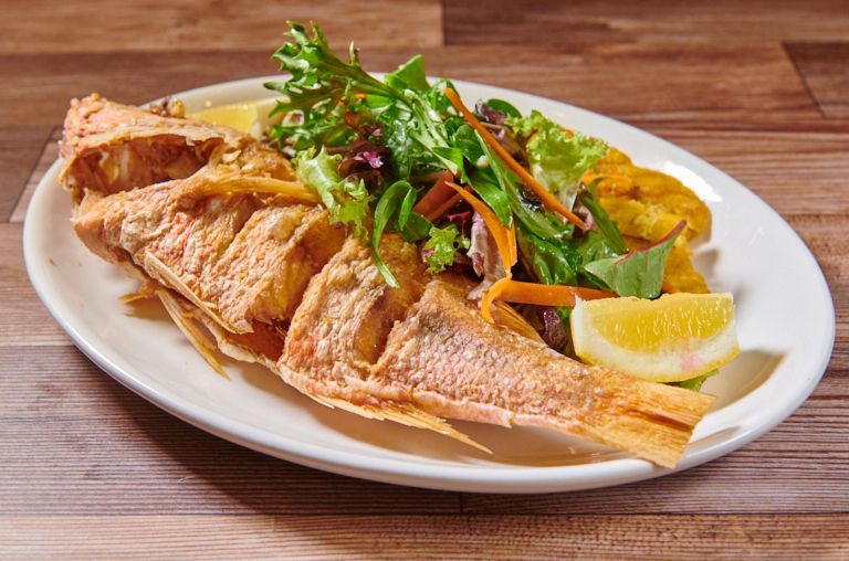 Fried whole fish with salad, plantains, and lemon wedge on a white plate.