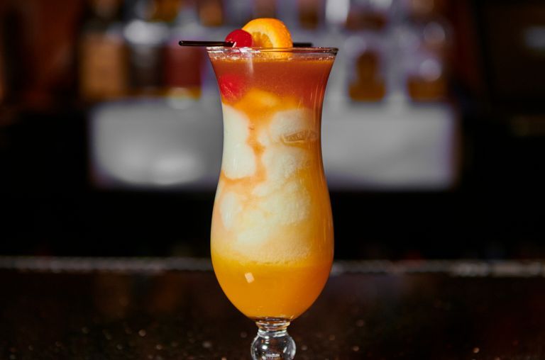 Layered tropical cocktail in a stemmed glass, garnished with cherry and orange slice.