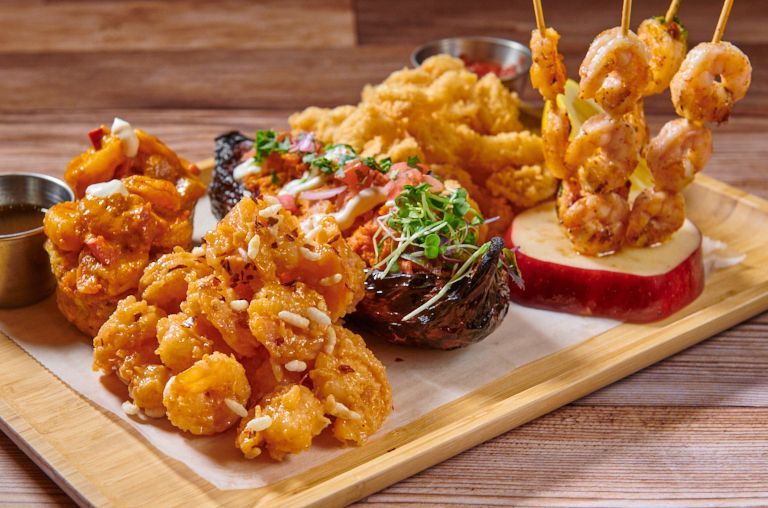 Fried shrimp appetizer platter with dipping sauces on a wooden board.