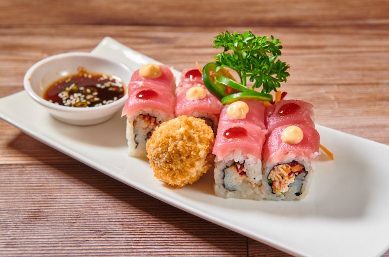 Sushi roll with tuna, sauce, and a fried item on a white plate.