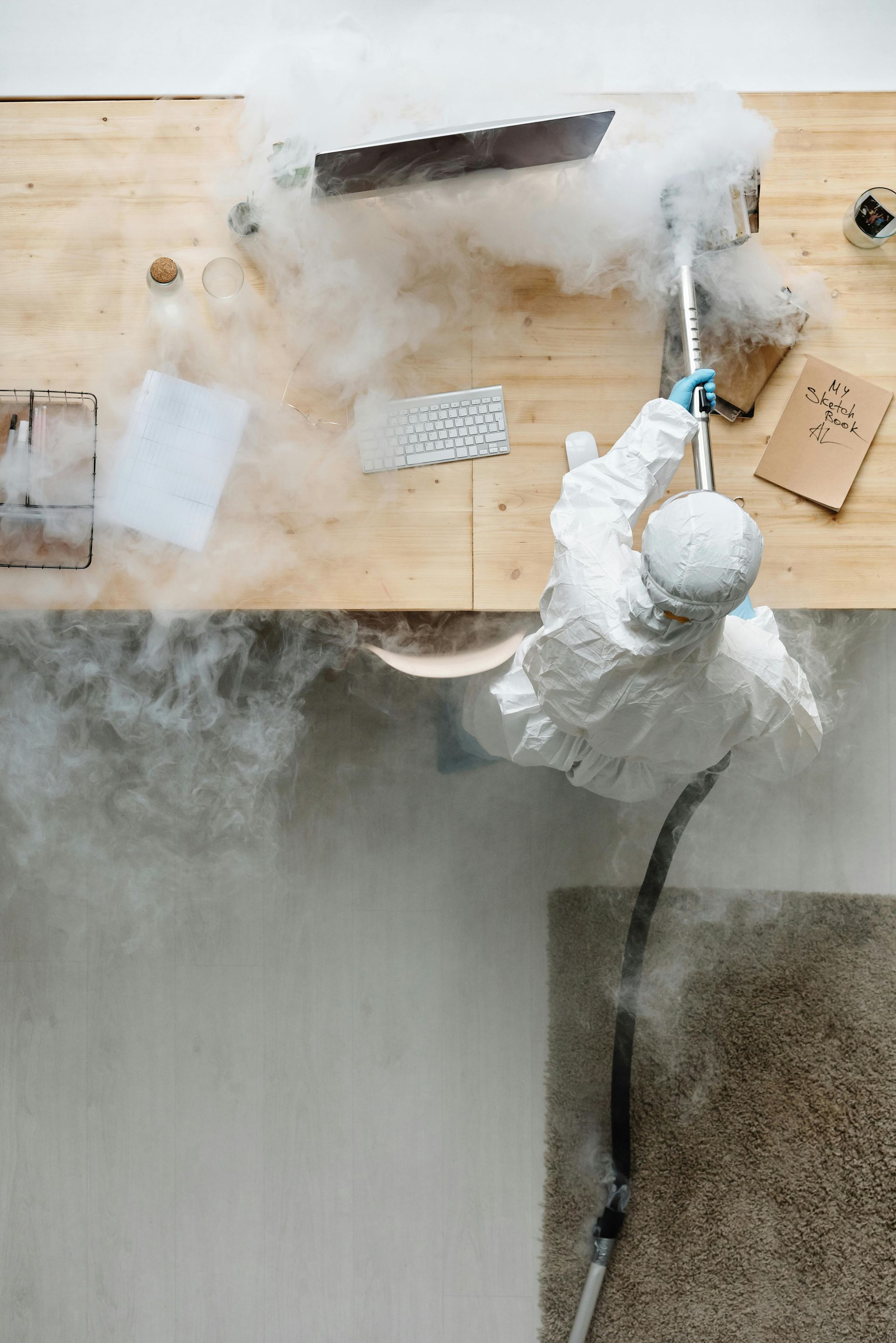 A man in a protective suit is cleaning a wooden table with a vacuum cleaner.