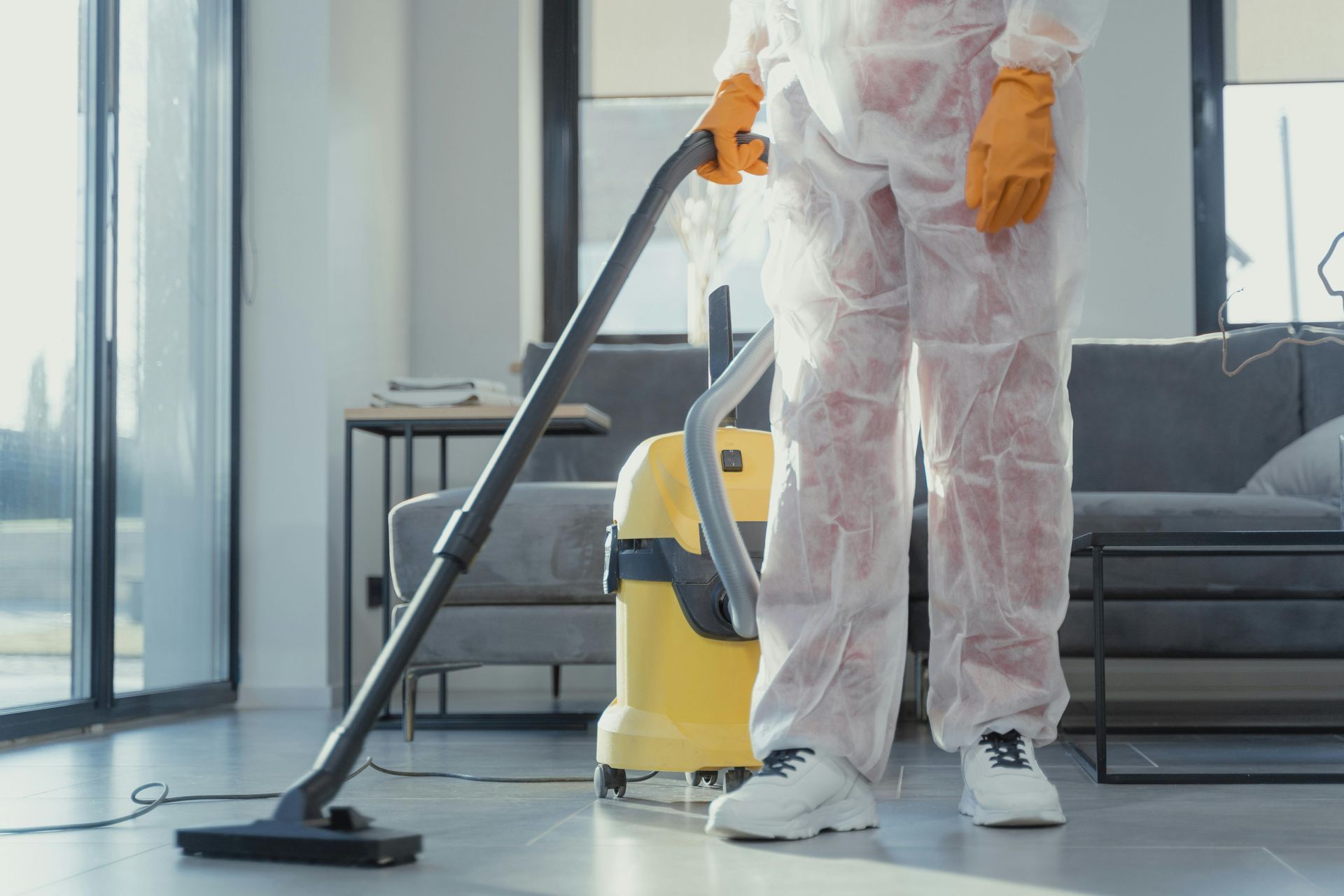 A person in a protective suit is using a vacuum cleaner in a living room.