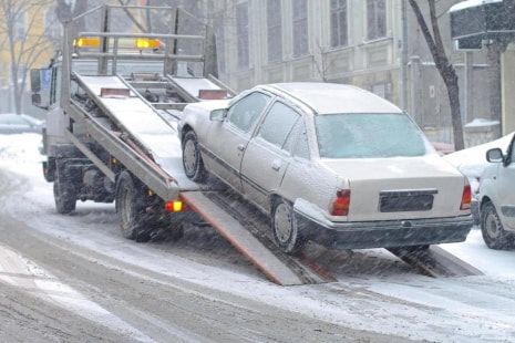 A car is being towed by a tow truck in the snow.