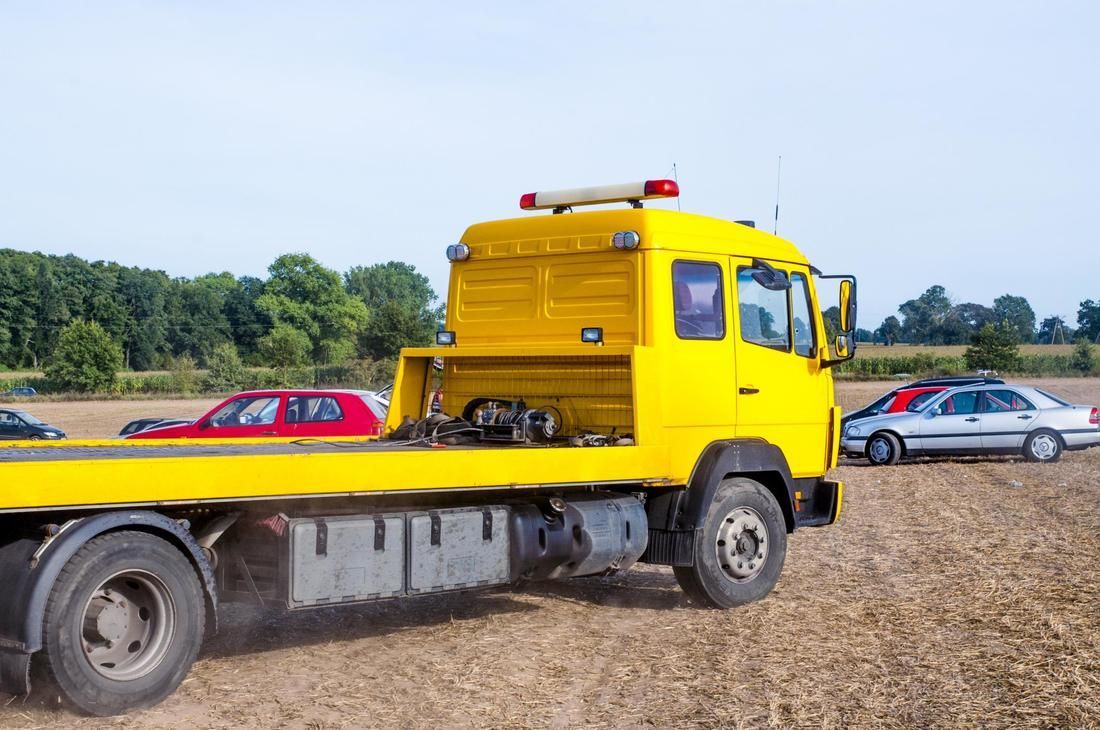 A yellow tow truck is towing a car in a field.