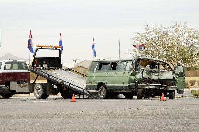 A green van is being towed by a tow truck.