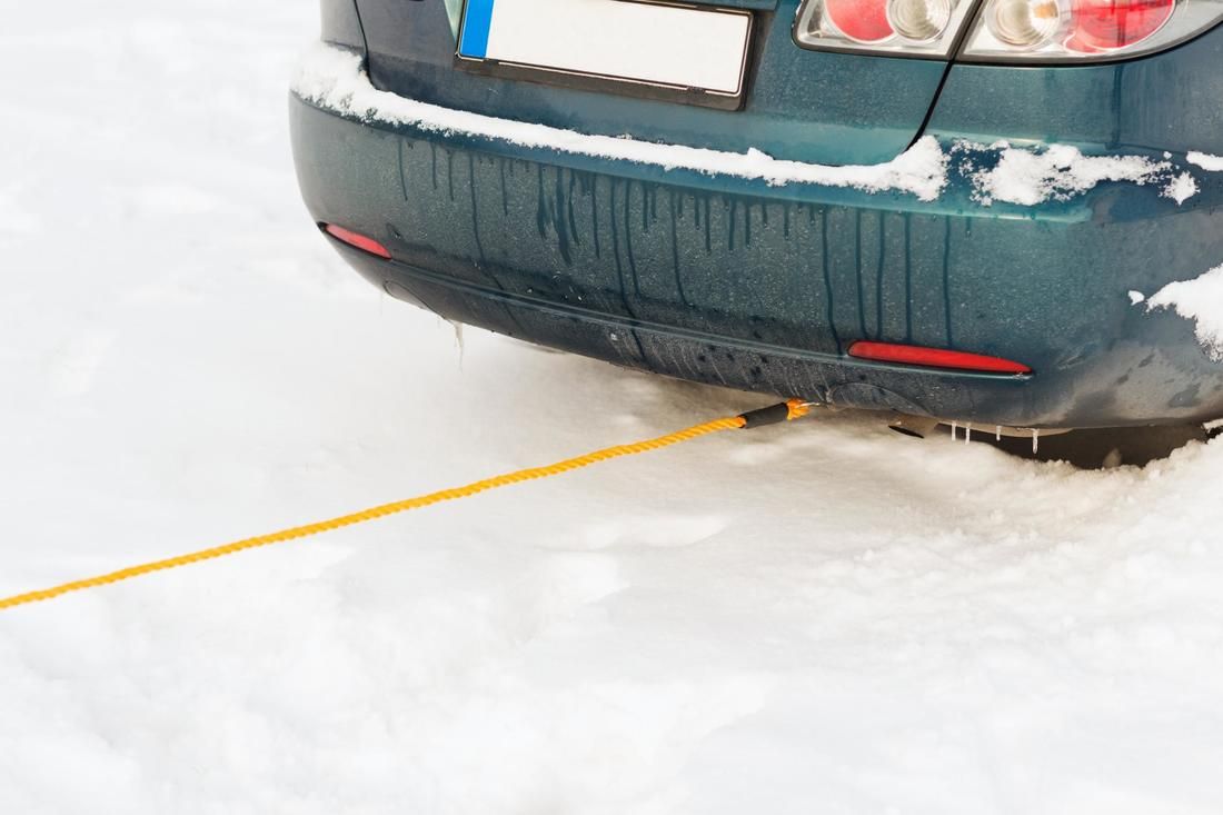 A car is stuck in the snow with a yellow tow line attached to it.