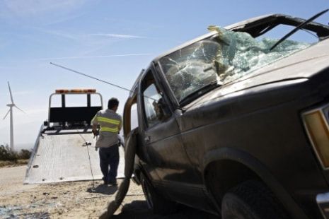 A man is standing next to a wrecked car on a tow truck.