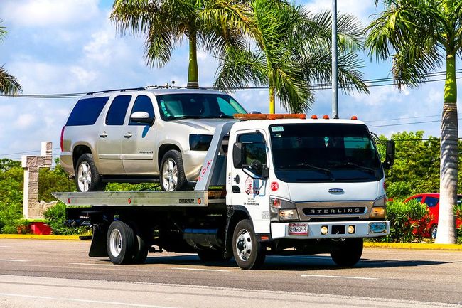 A tow truck is carrying a suv on the back of it.