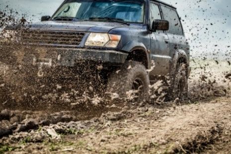 A suv is driving through a muddy field.