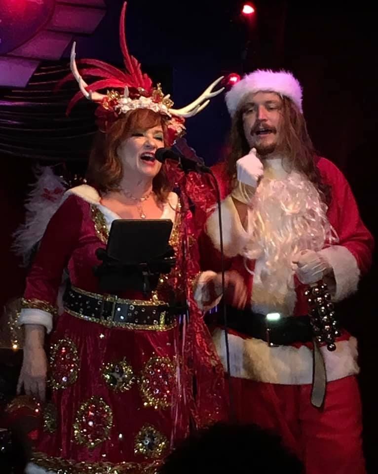 A man and a woman dressed as santa claus singing into microphones