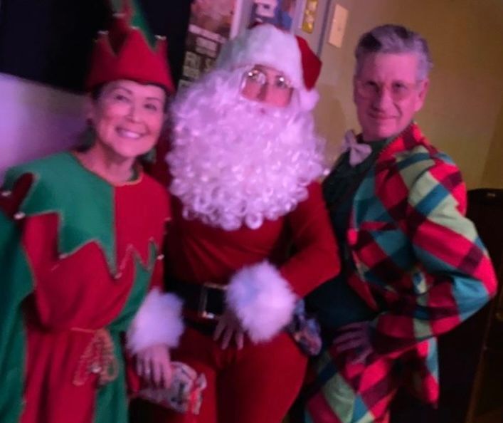 A man dressed as santa claus stands between two women dressed as elves