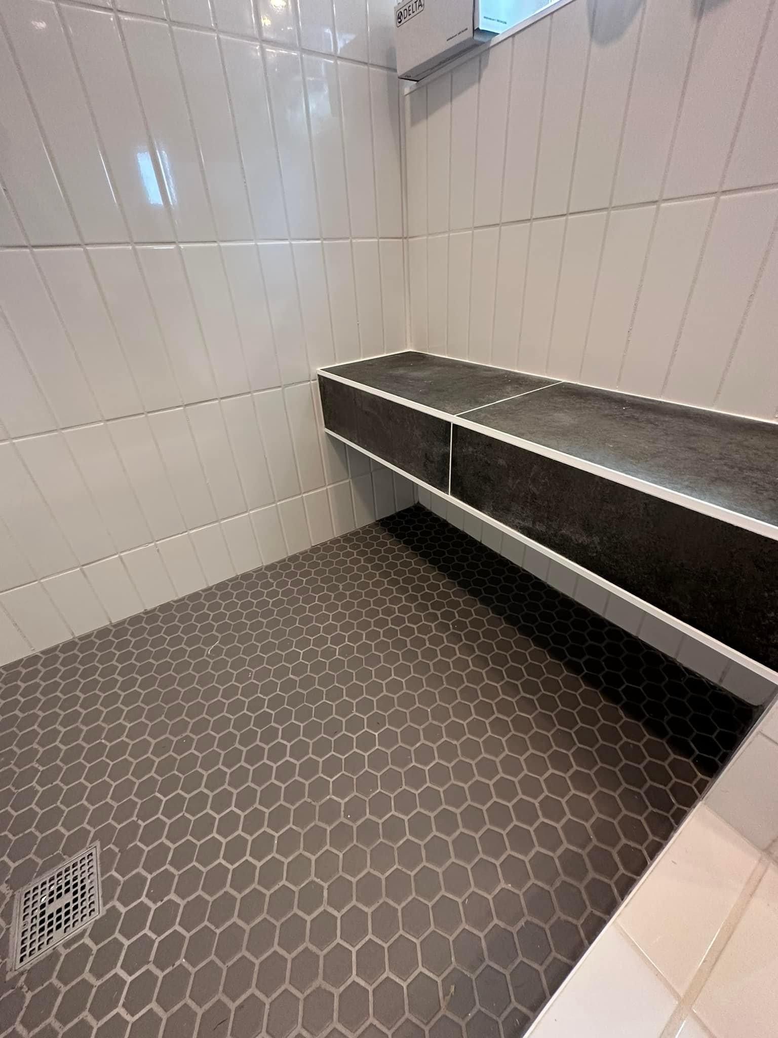 Shower tile remodel. White tile and gray floor mosaic and black tile bench. 