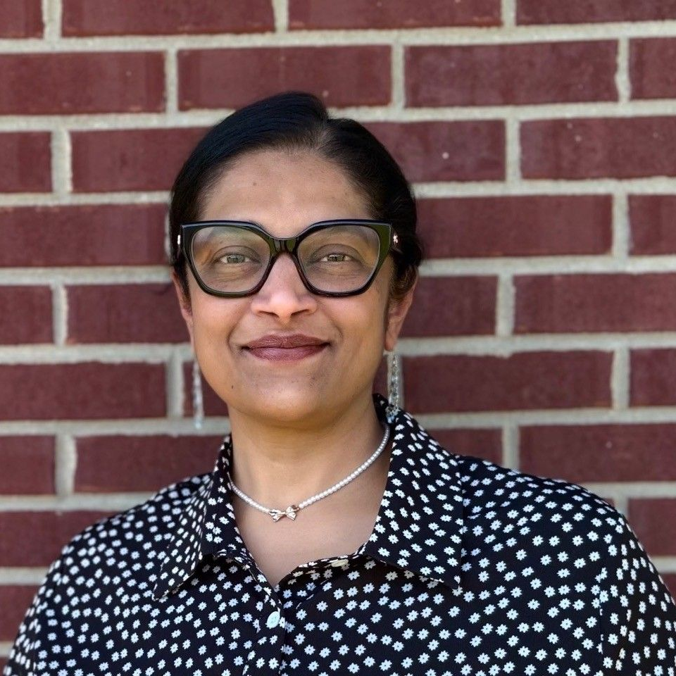 A woman in a black shirt is smiling in front of a brick wall.