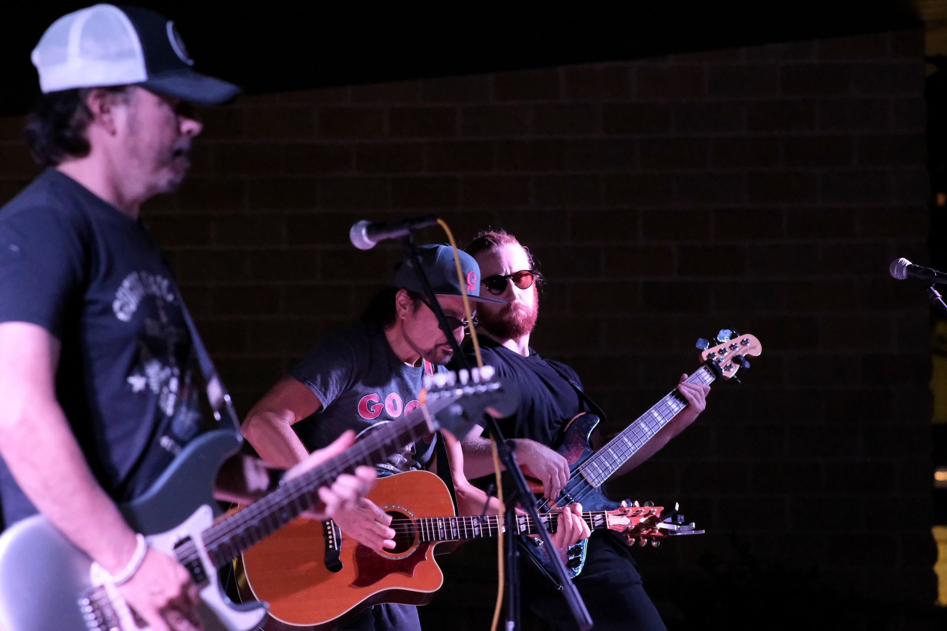 Band performing on stage, guitarist, singer with microphone and bassist, playing music at a venue.