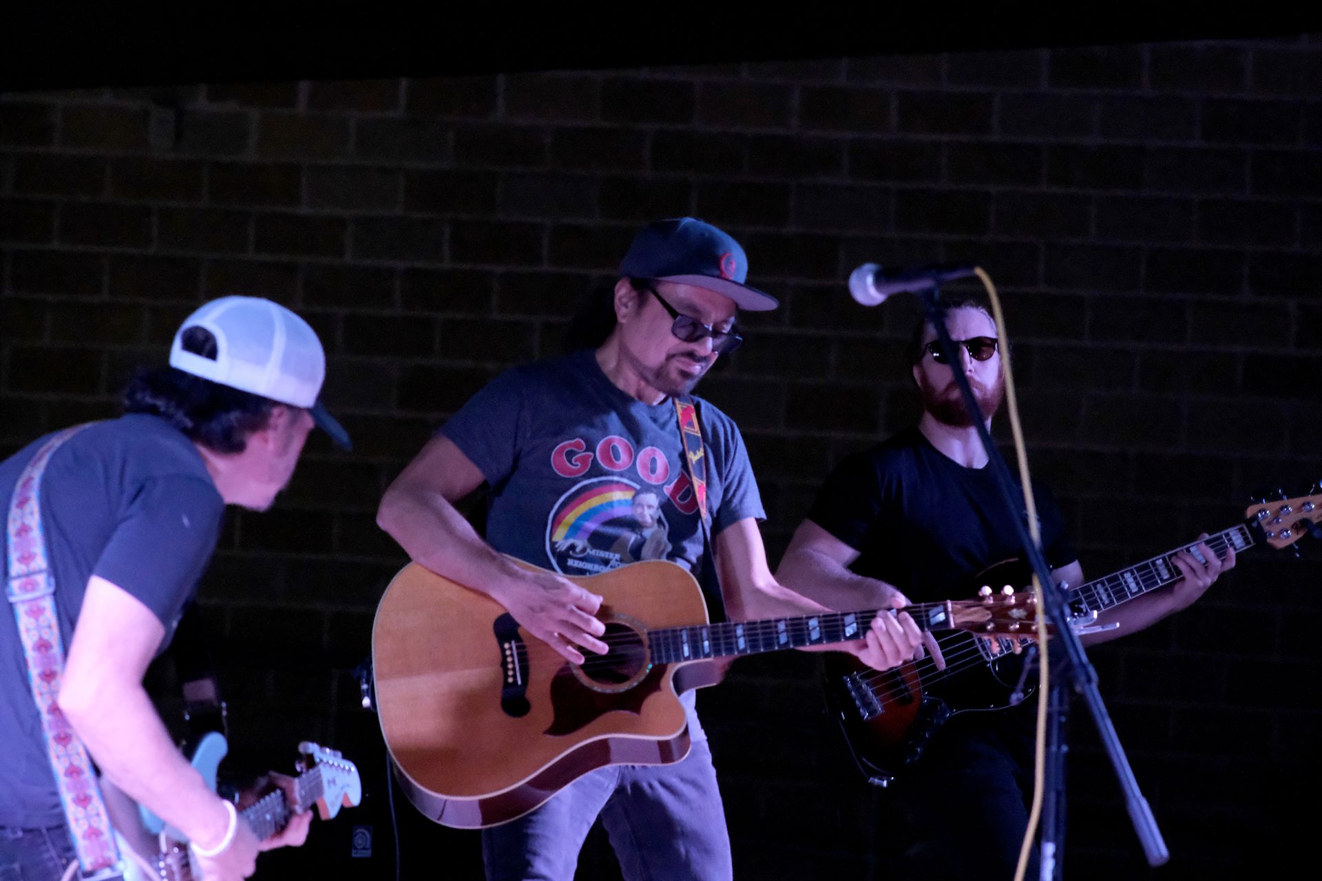 Band playing on stage: a guitarist in a cap singing into a microphone, flanked by two other guitarists.