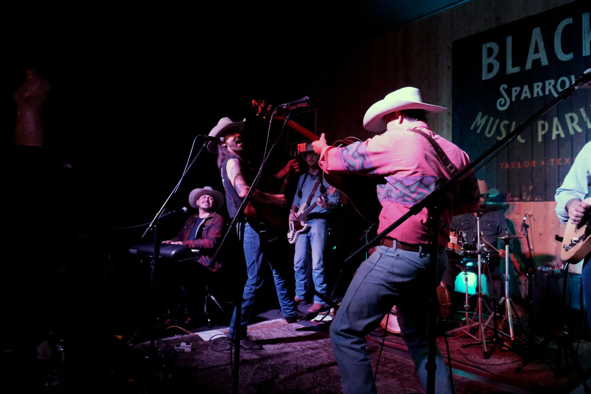 Band performing on stage at Black Sparrow Music Parlor. Musicians playing guitars, drums, and keyboard