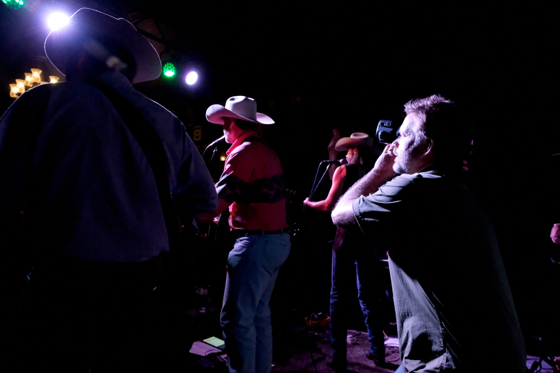 Band performing on a stage lit by spotlights, with a crowd watching.
