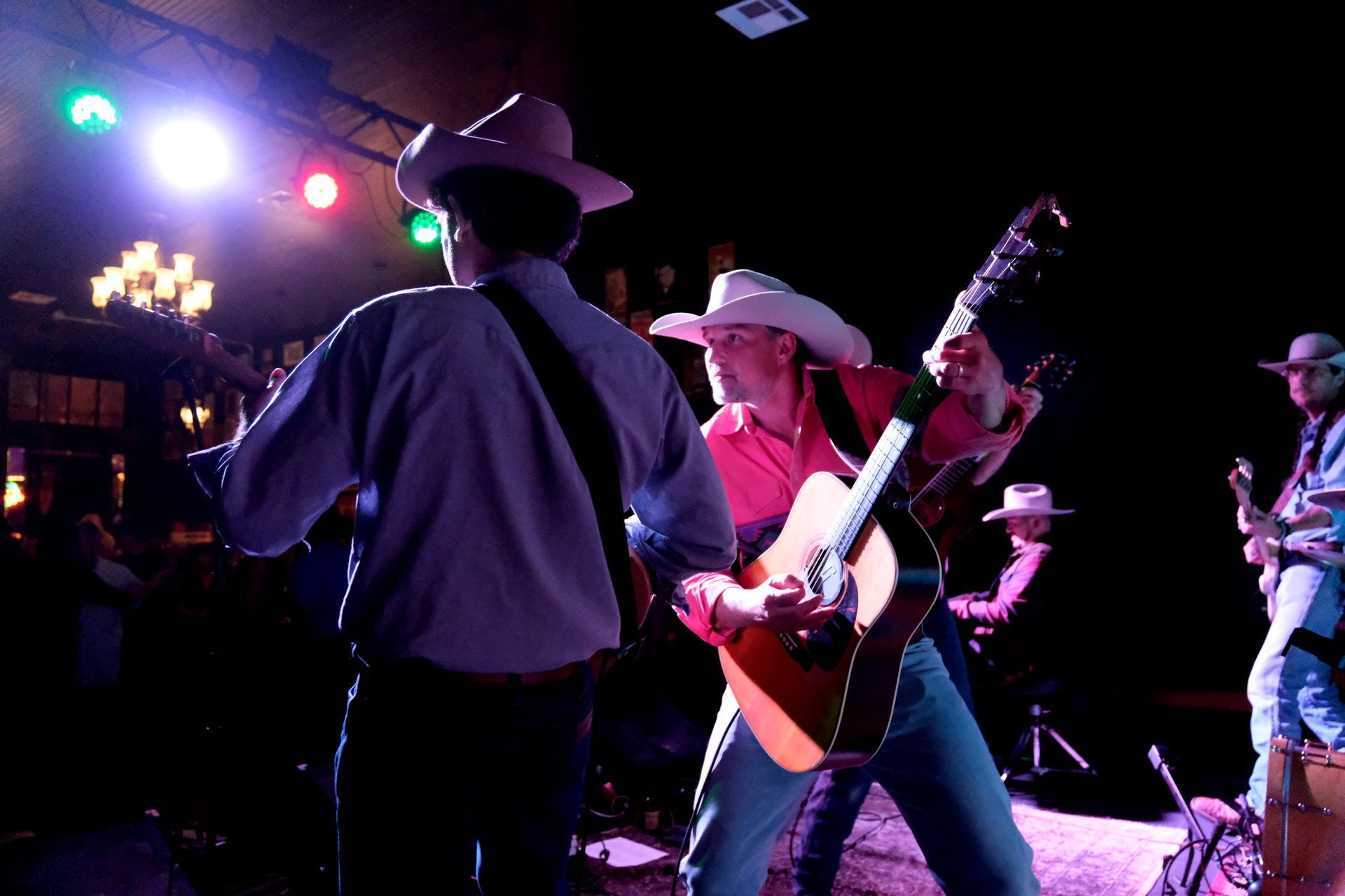 Country music band performing on stage, wearing cowboy hats and playing guitars under stage lights.