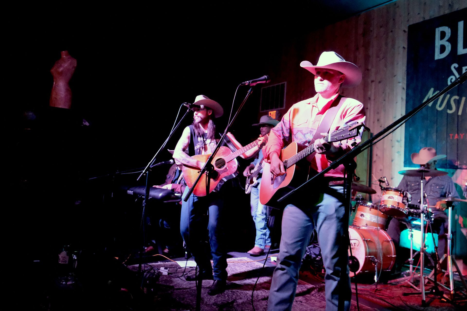 Band performing live on stage at a music venue, all wearing cowboy hats and playing instruments.
