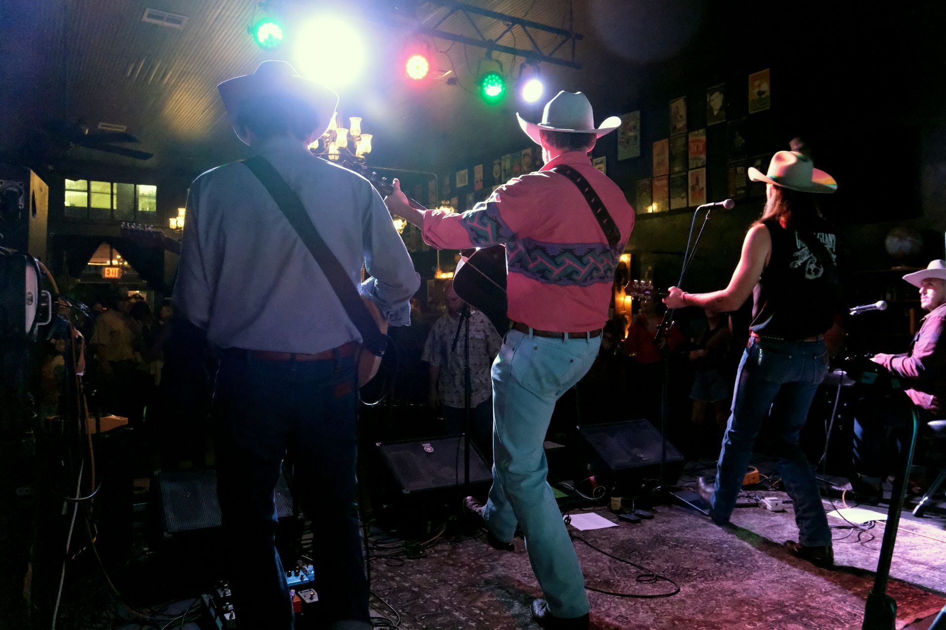 Band performing on stage in a dimly lit bar, musicians wearing cowboy hats, playing instruments.