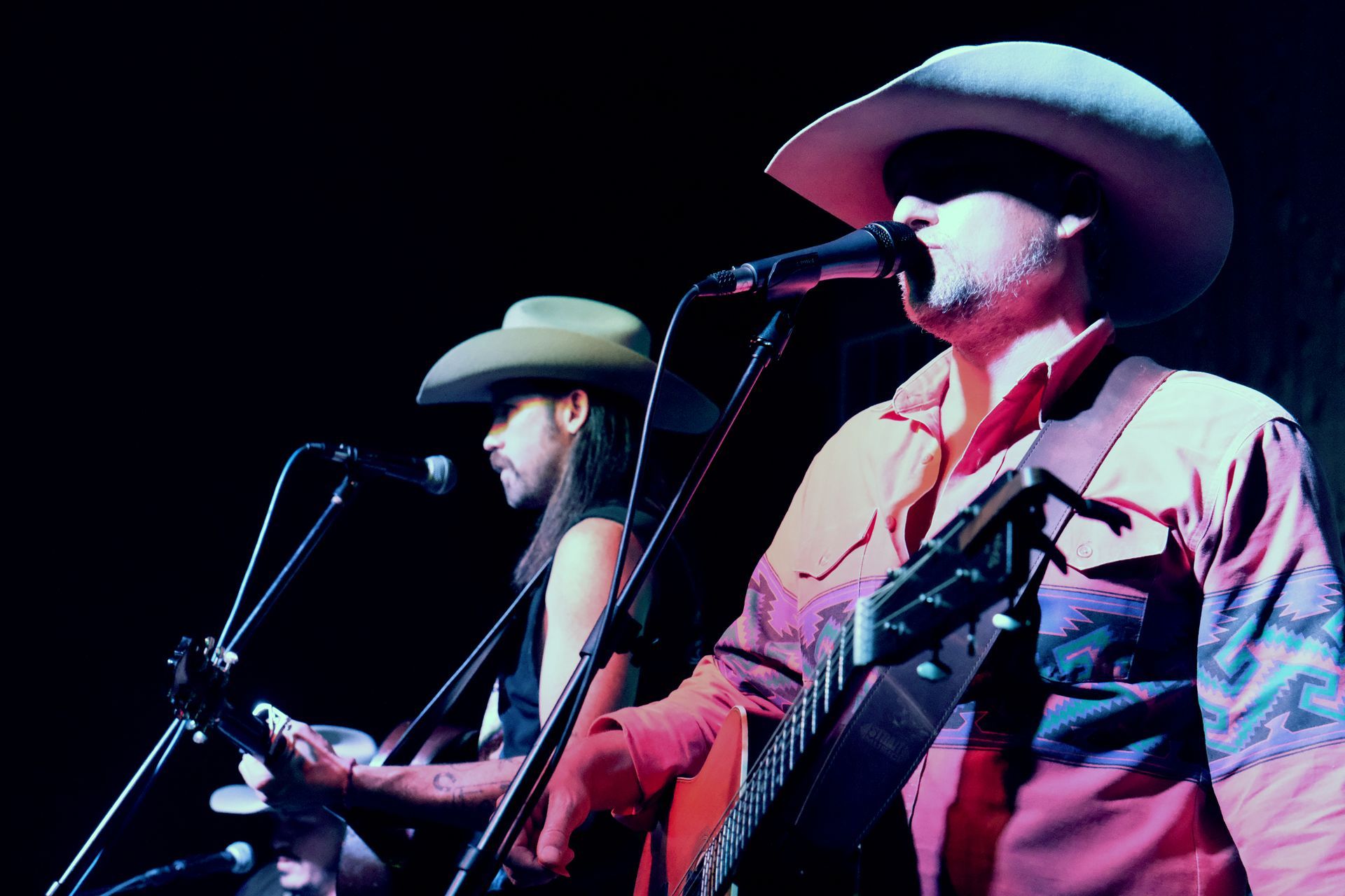 Two musicians in cowboy hats perform on stage, one plays guitar.