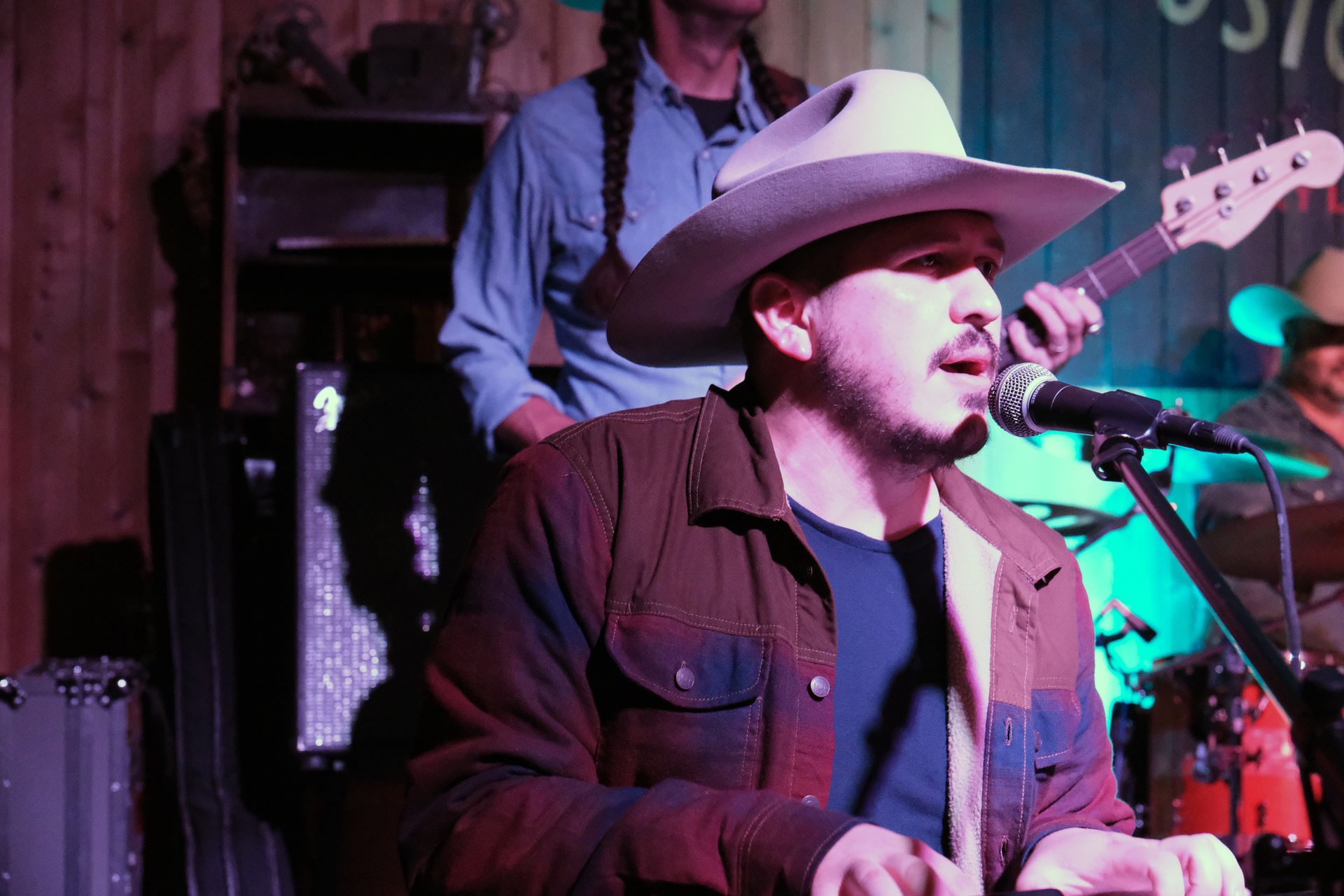 Man in cowboy hat singing into a microphone onstage with band.