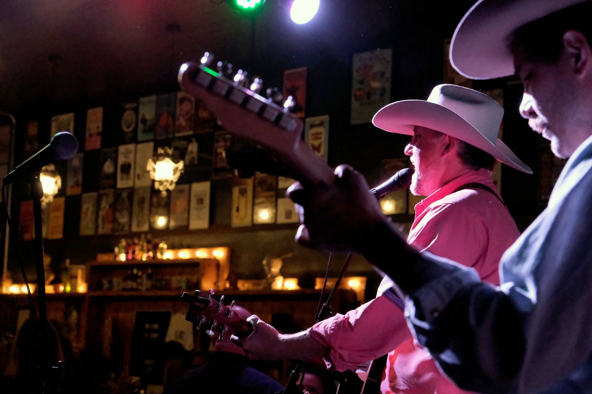 Two musicians in cowboy hats perform on stage, one plays guitar and sings, dim interior.